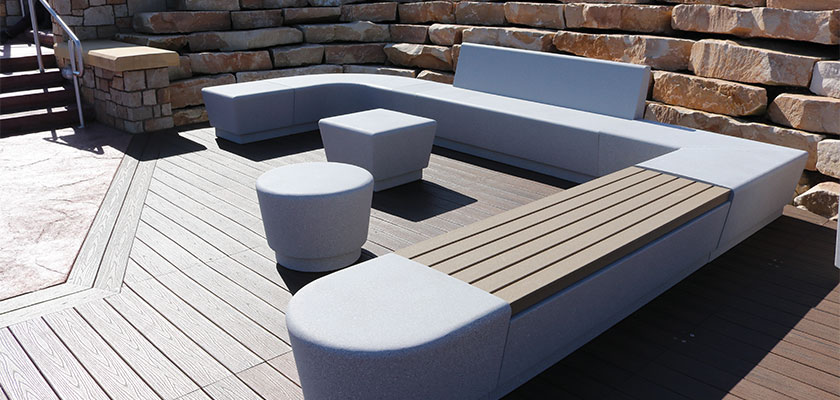 An asymmetrical U-shaped bench configured with white concrete pieces. Round and square footrests sit in the middle.