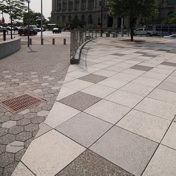 A city plaza divided by two types of terrazzo tile. There is light gray square terrazzo tile on the right and dark gray hexagonal tile on the left.