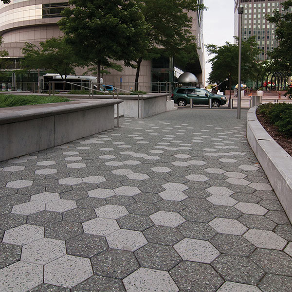 A city plaza with dark and light gray hexagon tiles covering the ground in front of a small set of stairs.