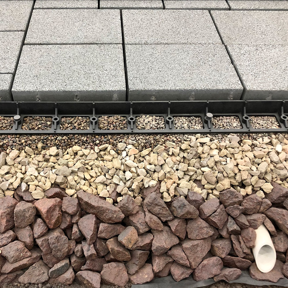 Rectangular, gray permeable pavers are lined up next to rocks.