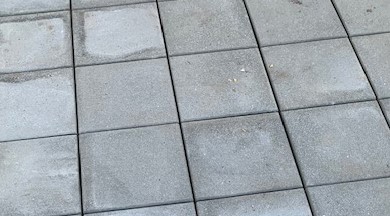 Gray square concrete pavers with lighter discolored areas of efflorescence.