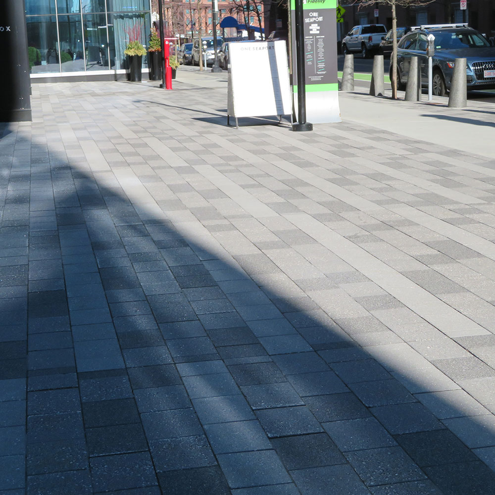 Grey pavers are located on an outdoor walkway located next to a street.