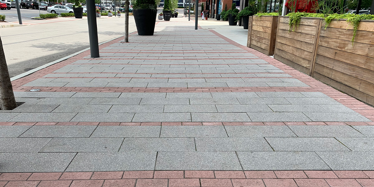 This walkway features gray and red pavers. There is a parking lot across the street.