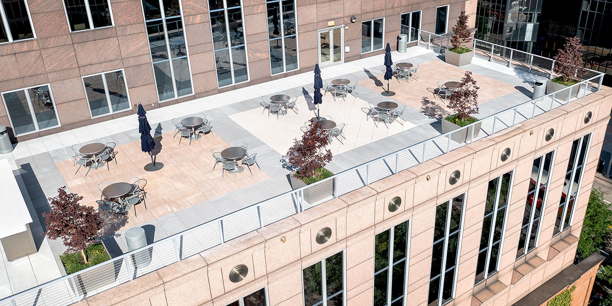 This building has a roof deck with various round tables, chairs, plants and umbrellas.