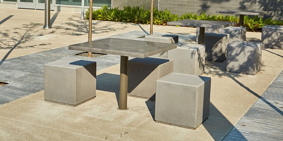 A courtyard with a metal table surrounded by three cube-shaped concrete seats.