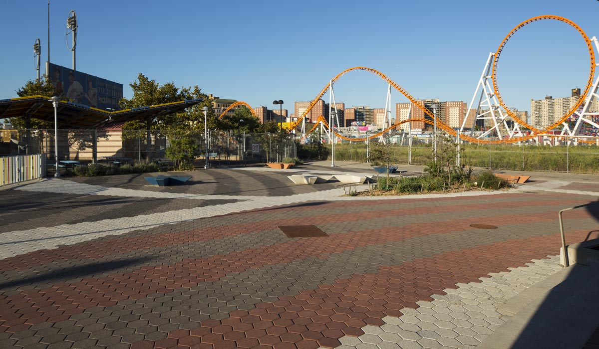 This outdoor area has red, white and gray pavers. There is a rollercoaster in the background.